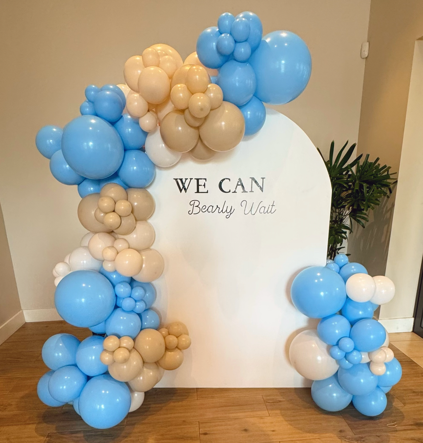 Blue, beige, and white balloon arch around a white sign that says