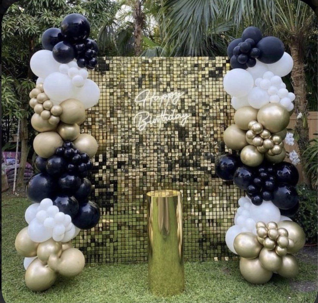 Birthday backdrop with gold sequins, balloons in black, white, and gold, and gold pedestal.