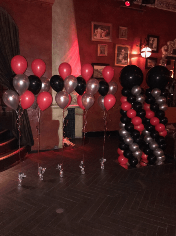 Red, black, and silver balloons decorate an interior space with dim red lighting.