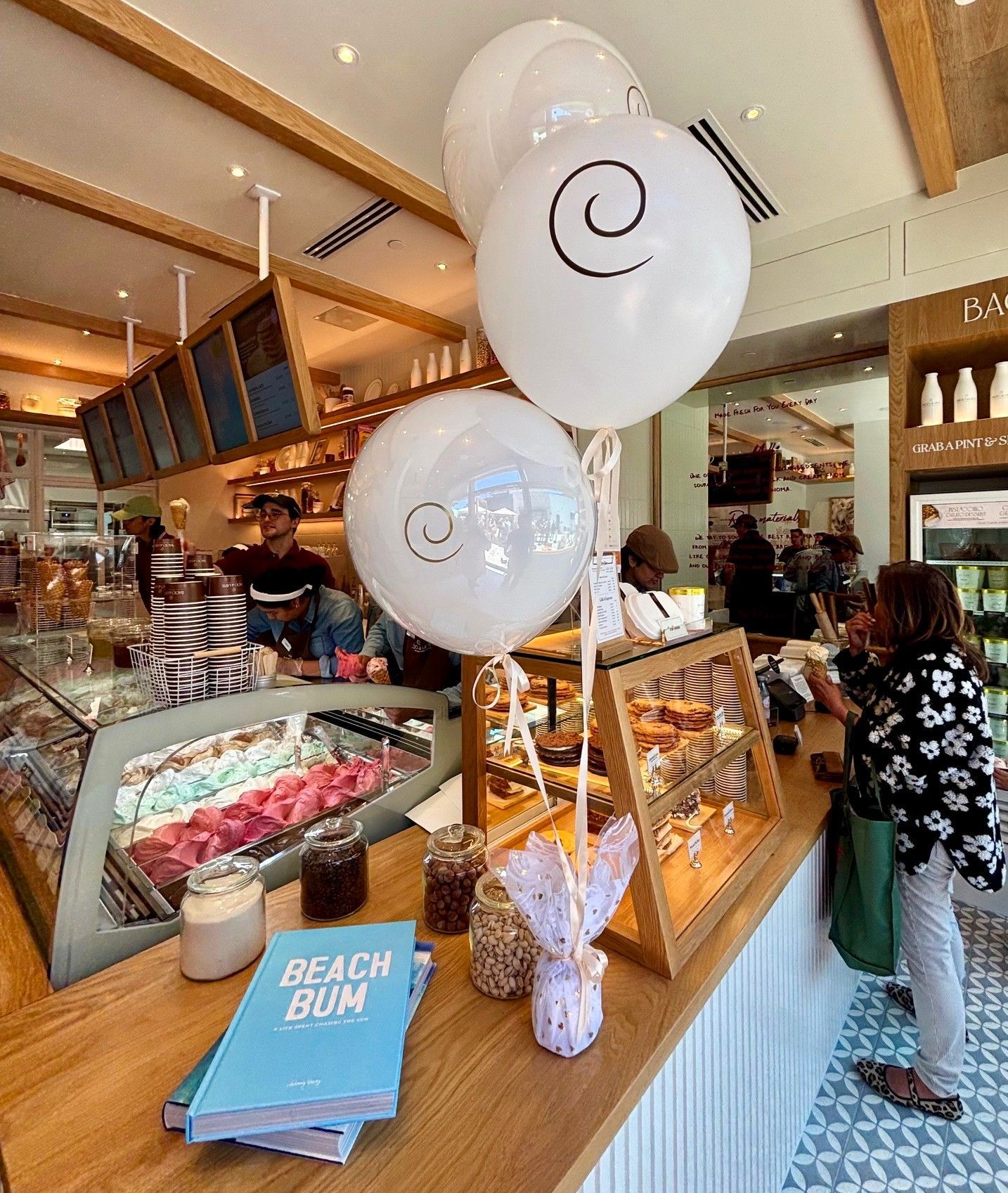 Branded balloon bouquet on the counter inside Bacio di Latte Manhattan Beach as staff scoop gelato for customers