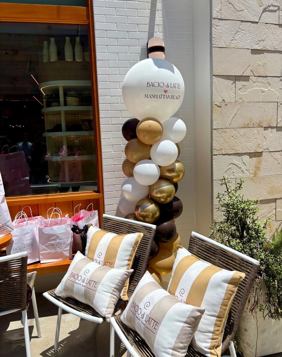 Branded balloon column beside the Bacio di Latte merchandise table, its printed logo topper matching the logo on the giveaway pillows and merch