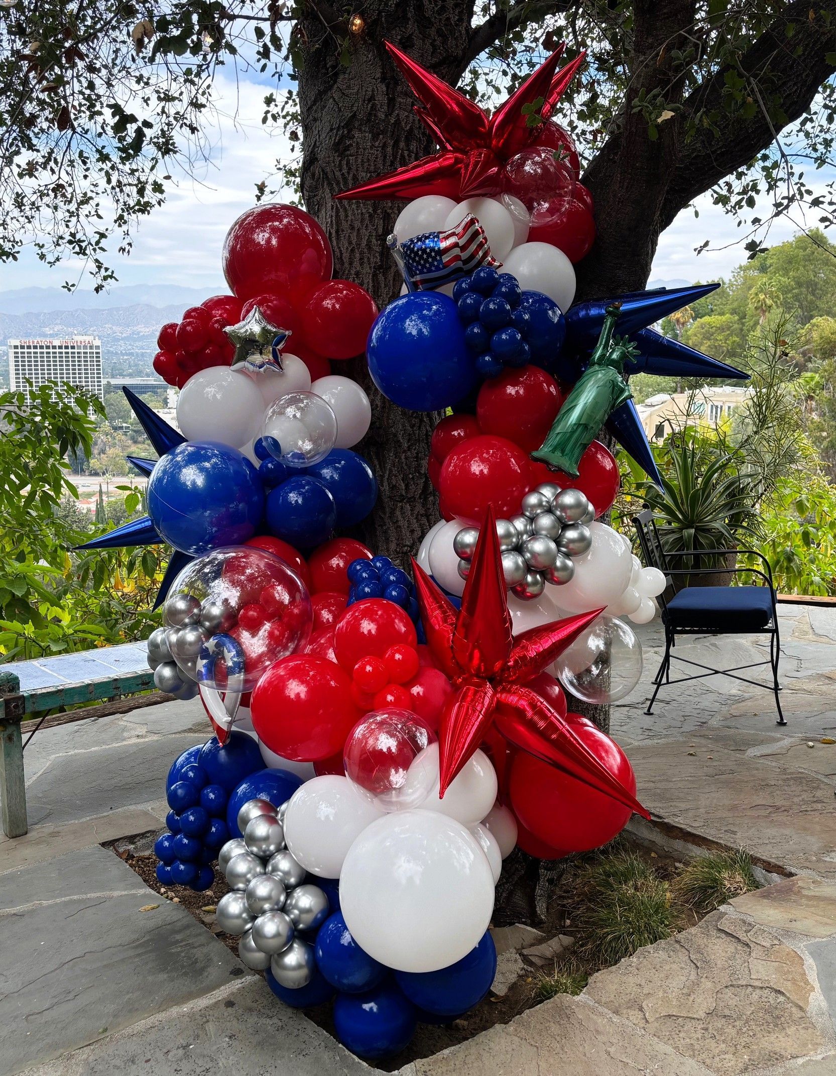 Red, white and blue organic balloon installation wrapped around a backyard tree with metallic spikes, clear bubble balloons and Fourth of July accents