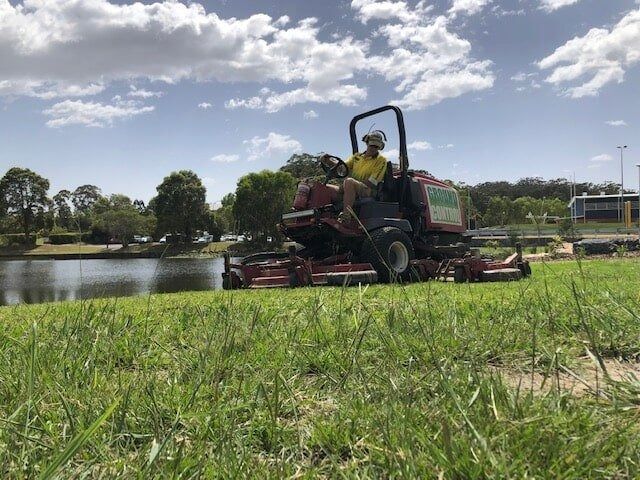 Man Operating a Red Lawnmower — Ground Control Property Maintenance In North Boambee Valley, NSW