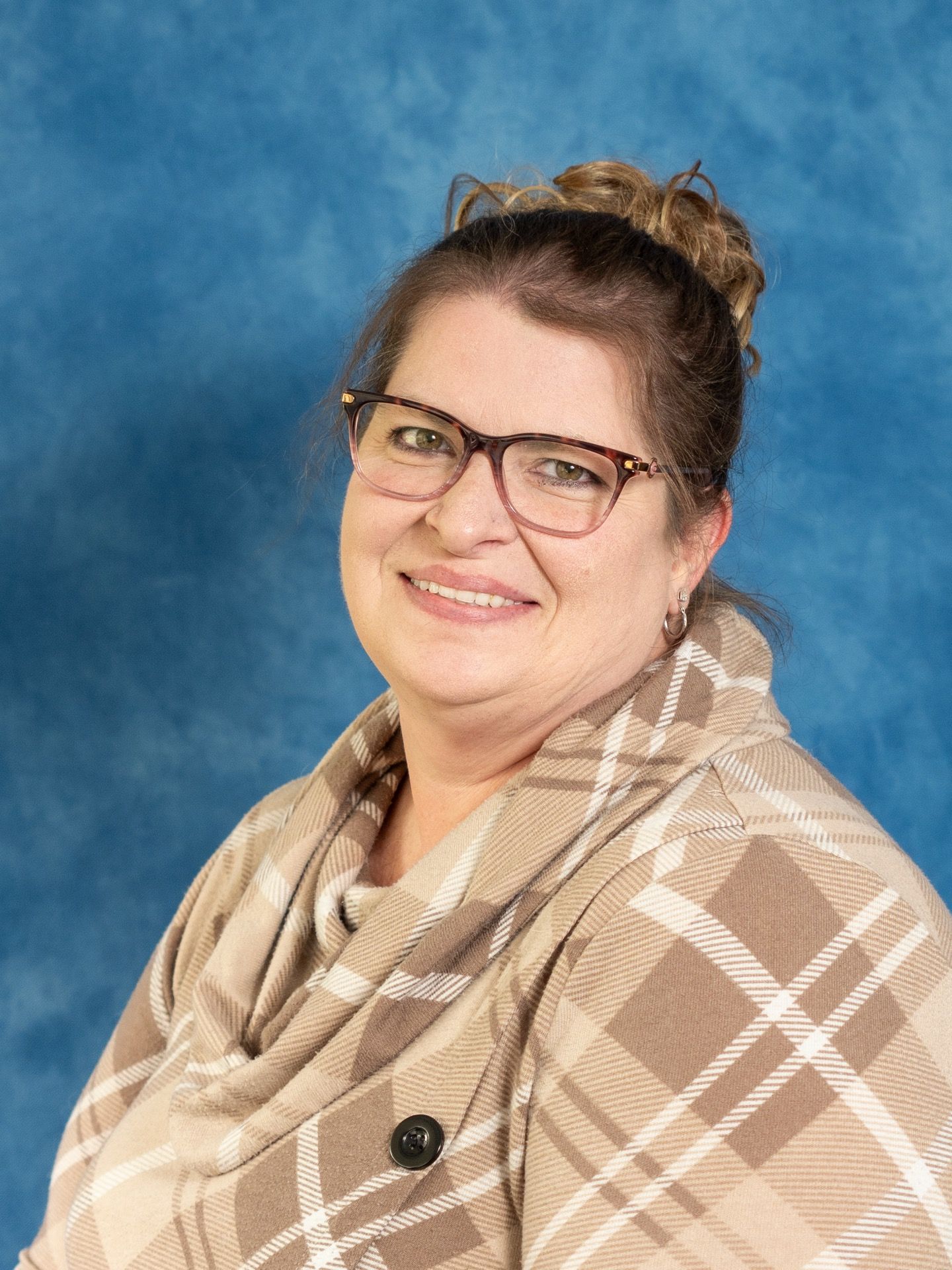Smiling woman wearing glasses and a beige plaid scarf against a blue studio backdrop