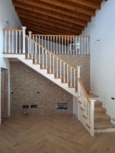 Interni moderni con soffitto con travi a vista, pareti in mattoni e una scala con ringhiere bianche.
