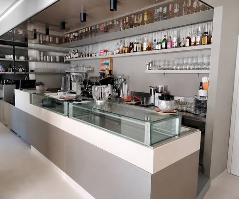 Moderno bancone bar con vetrina, scaffali per bottiglie e attrezzatura per il caffè in un luminoso interno di caffetteria.