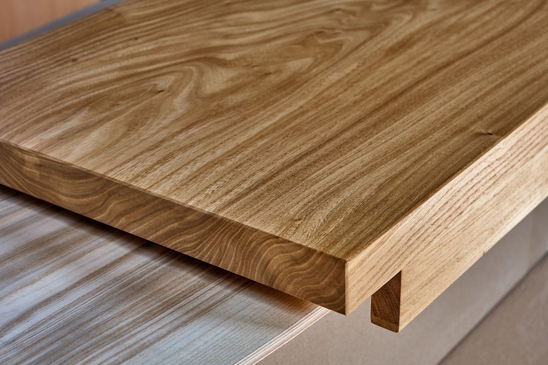 Primo piano di un piano di tavolo in legno con bordo smussato e venature ben visibili.