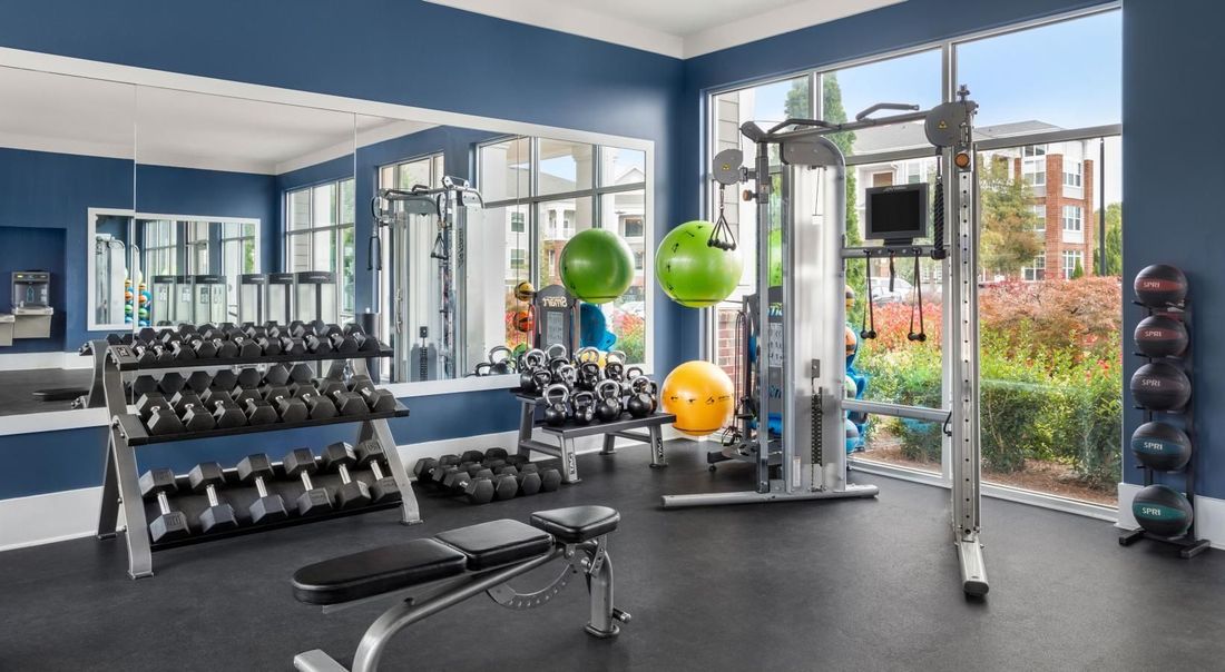 A gym with a lot of dumbbells , a bench , and a large window.