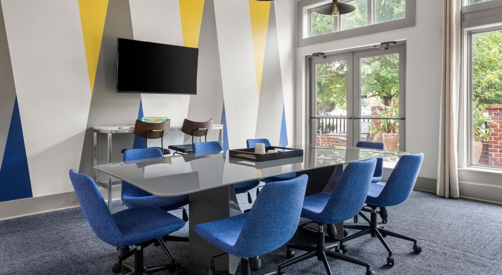 A conference room with a long table and blue chairs and a flat screen tv.