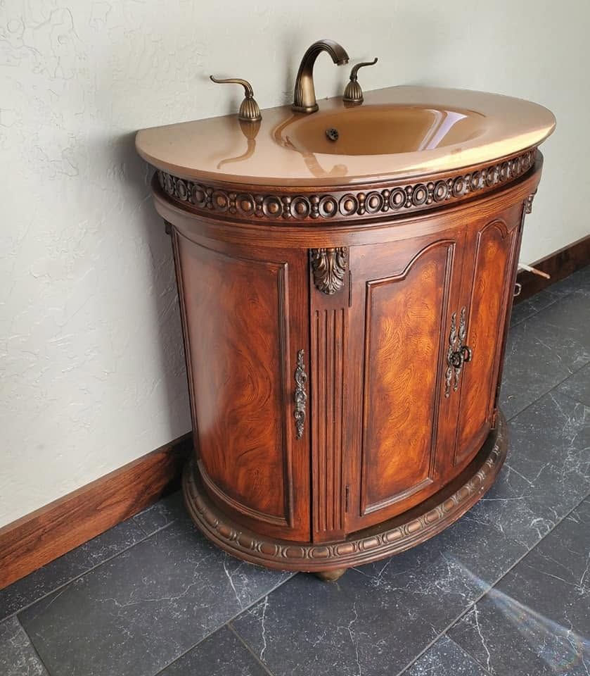 Ornate wooden bathroom vanity with copper sink and bronze faucet on a dark tile floor