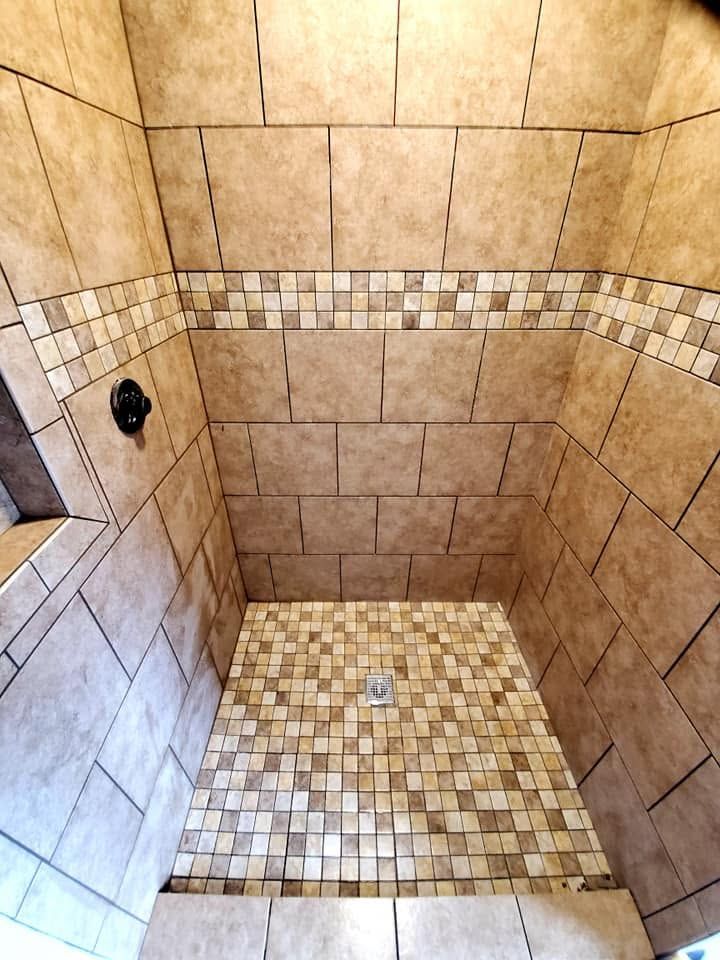 Empty beige-tiled shower stall with a mosaic tile floor and a single wall fixture