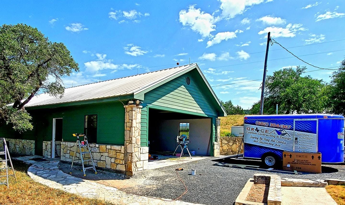 Green building with a metal roof beside a blue trailer under a bright blue sky