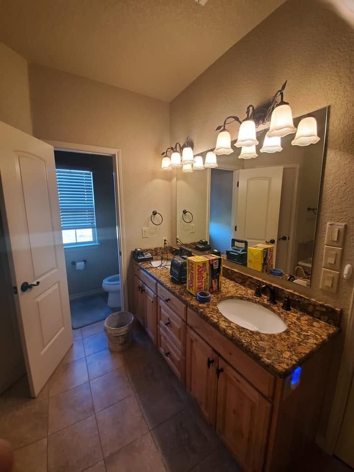 Bathroom with double sink vanity, granite countertop, mirror lights, and open door to toilet area.