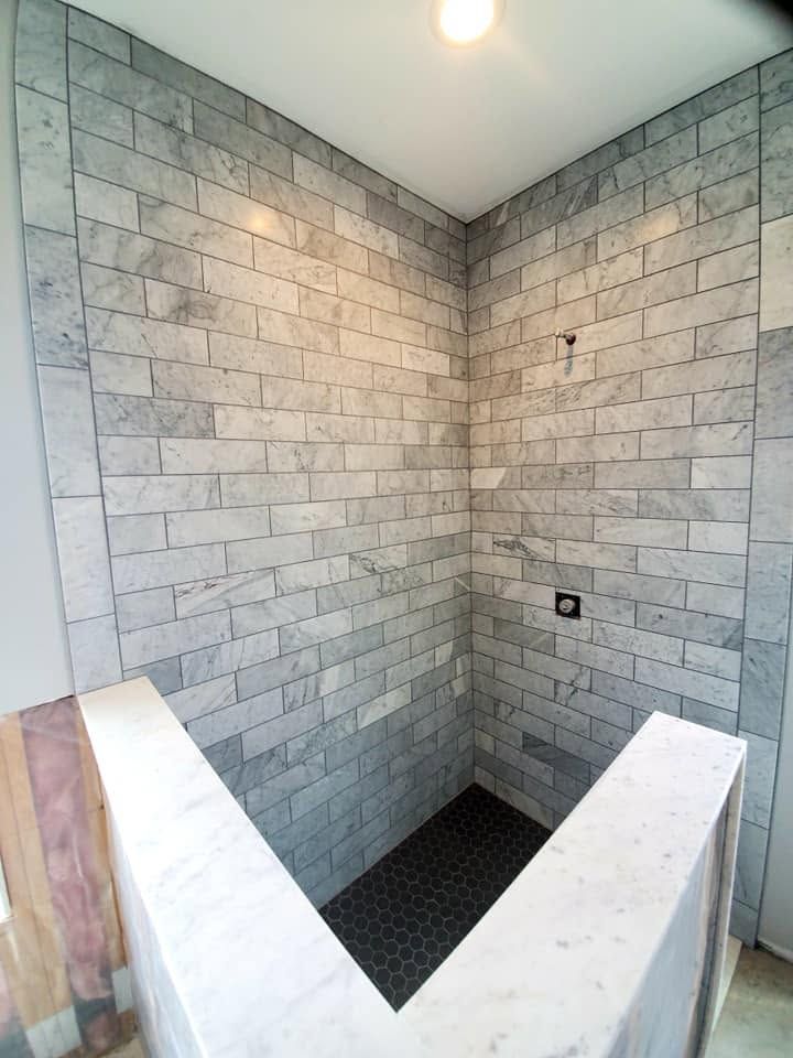 Partially tiled shower alcove with gray stone walls and a dark floor, viewed from the entrance