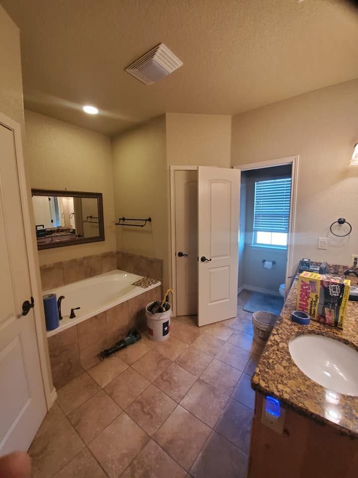 Bathroom with a white tub, granite vanity, tan tile floor, and a window with blue blinds.