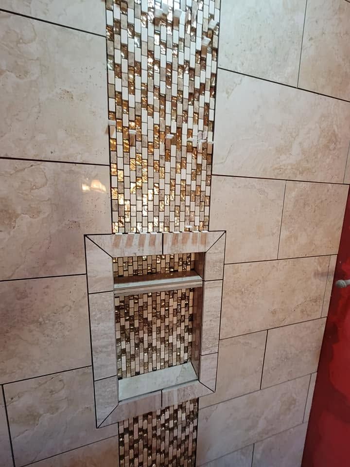 Decorative wall niche with mosaic tiles and a small glass shelf on a beige tiled wall