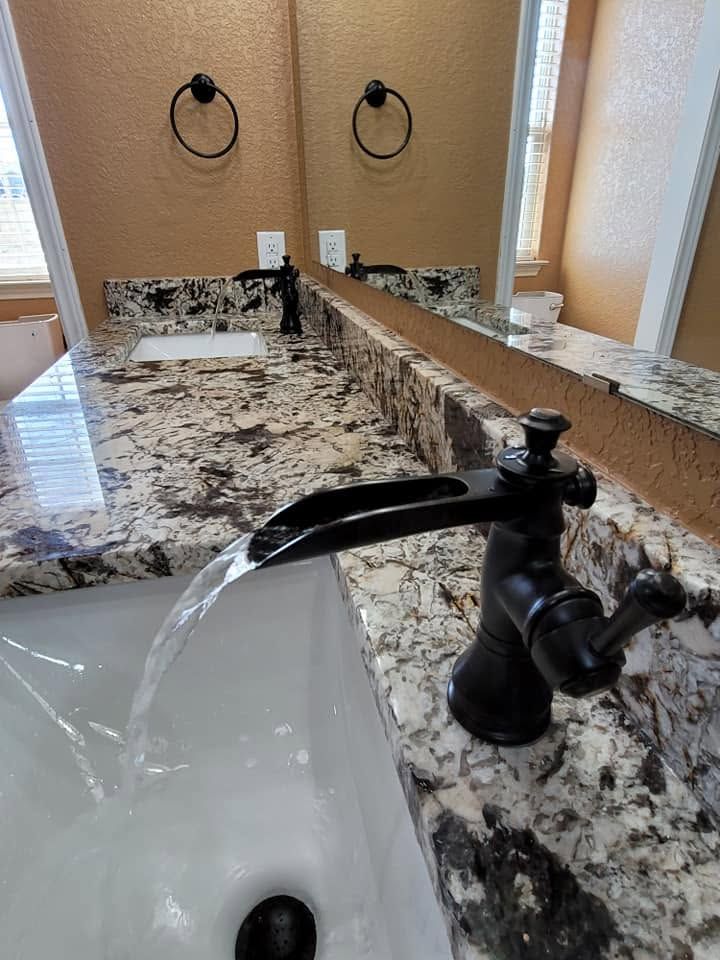 Bathroom vanity with granite countertop, black faucet, and sink mirror reflection