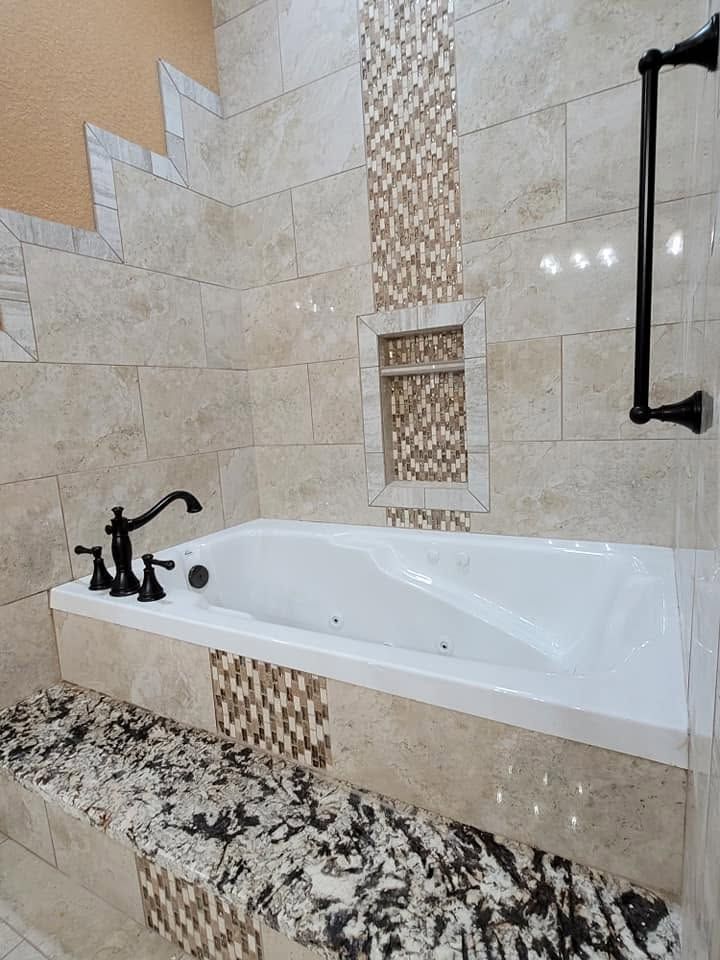 Modern beige-tiled bathroom with a white soaking tub and granite counter.