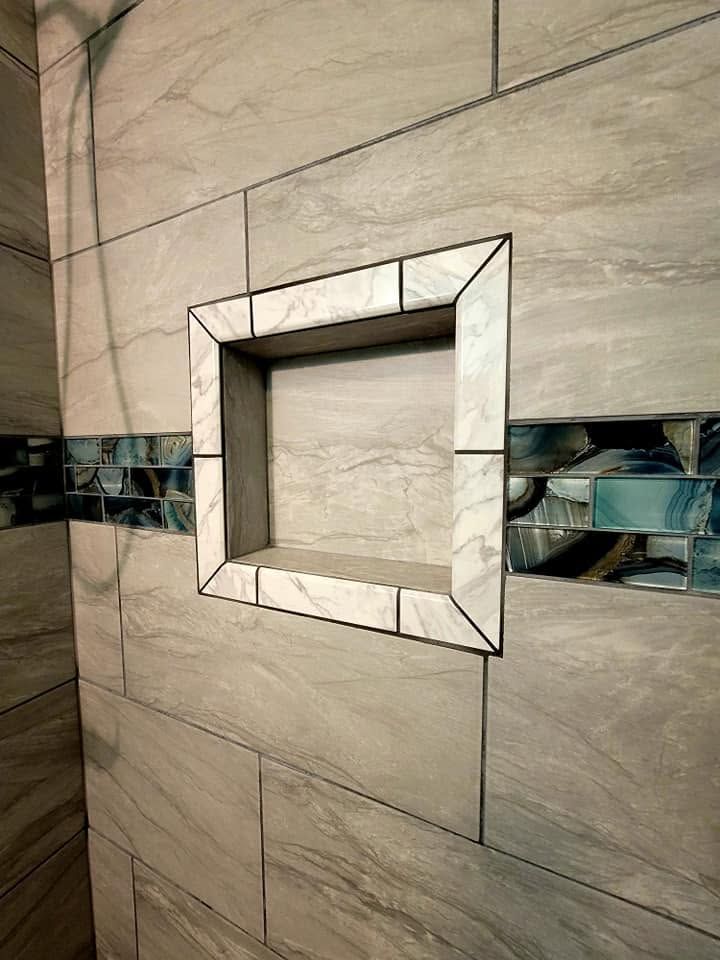 Empty square wall niche with mirrored trim and gray stone tiles, crossed by a dark decorative strip
