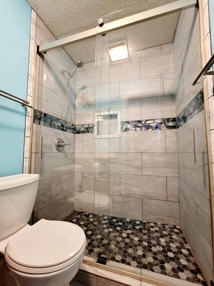Small tiled shower stall with glass doors, mosaic floor, and toilet in the foreground.