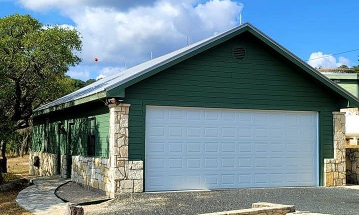 Single-story green garage with white double door and stone trim under a blue sky