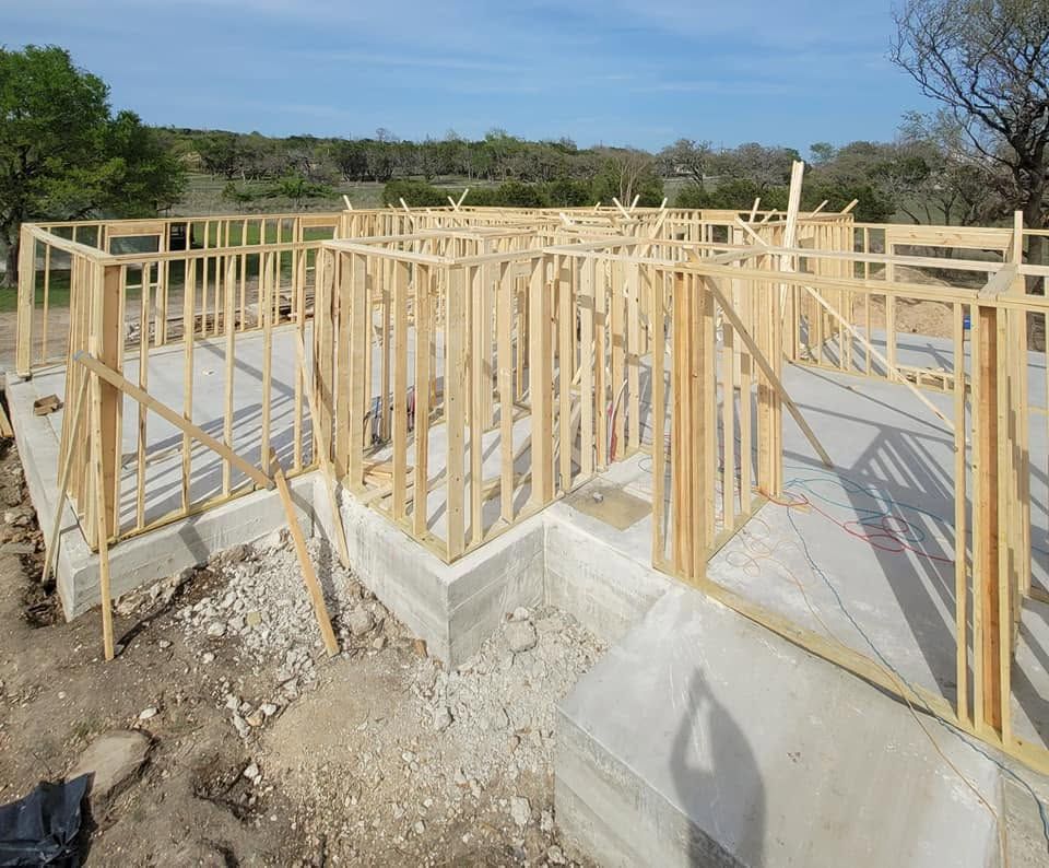 Wooden house framing on a concrete foundation at a construction site under a clear sky