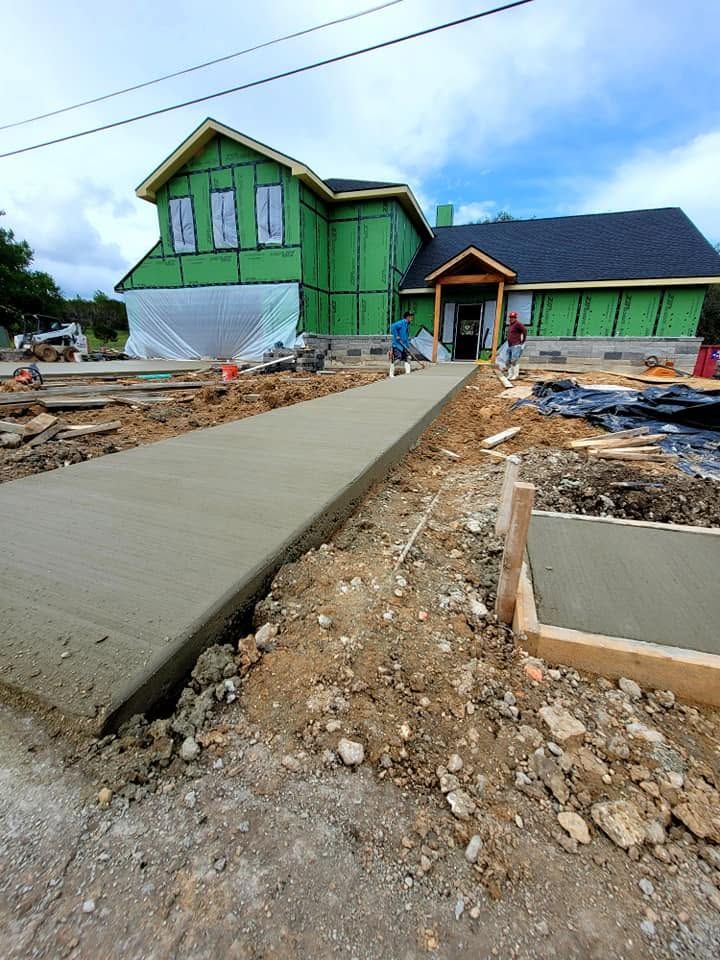 Concrete walkway leading to a green house under construction with exposed dirt and building materials