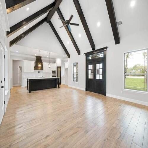 Custom home great room with vaulted ceiling, exposed beams, black kitchen island and hardwood floors