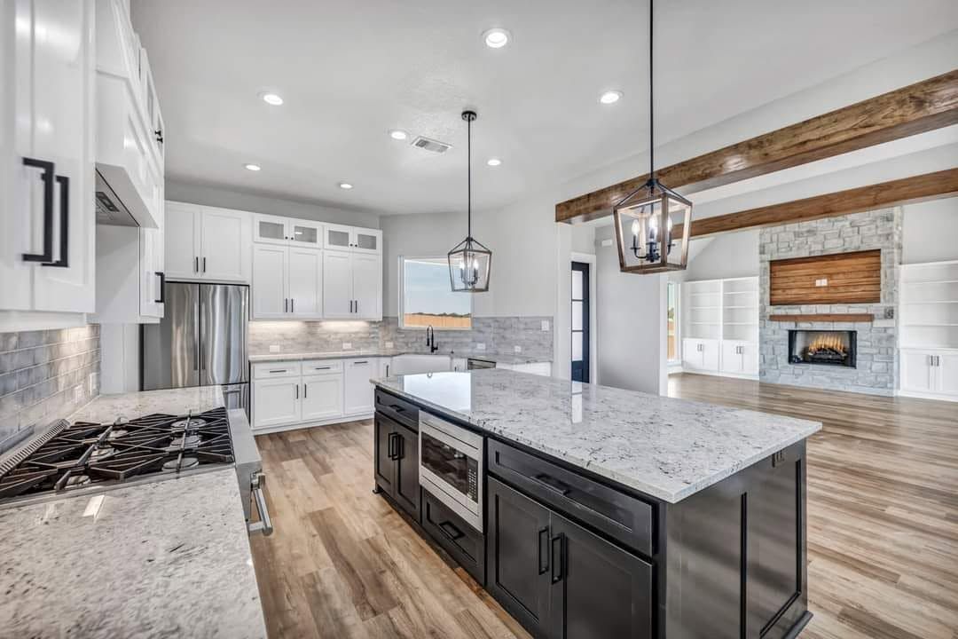 Bright modern kitchen with white cabinets, marble island, pendant lights, and wood floors