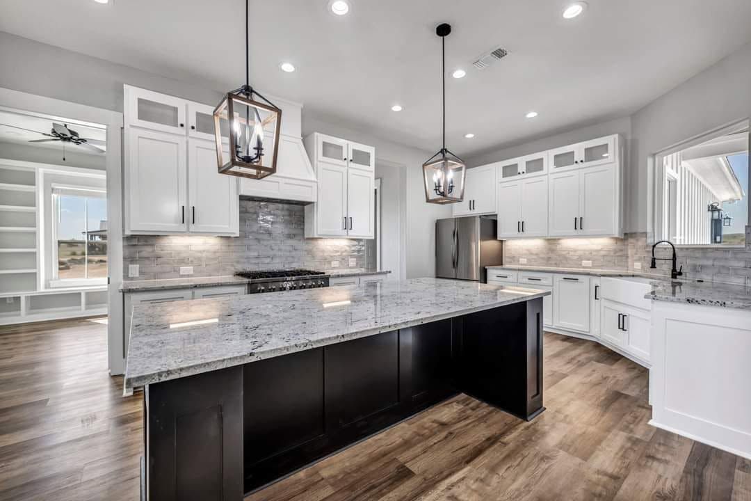 Modern white kitchen with black island, pendant lights, stainless appliances, and wood floors