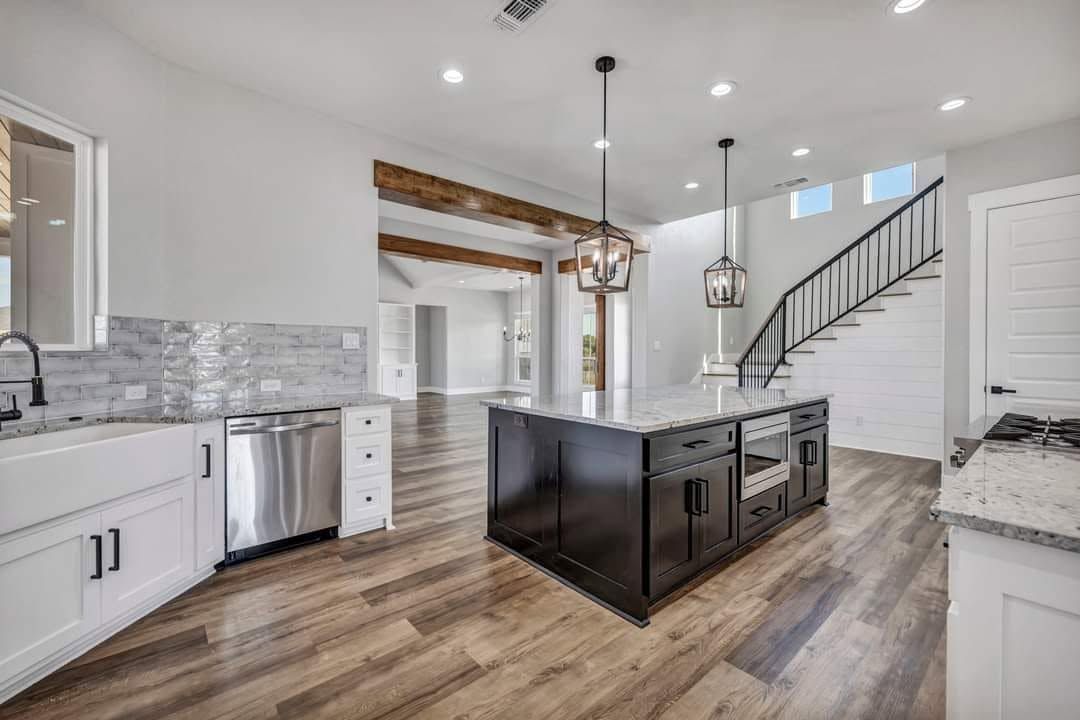 Bright modern kitchen with black island, white cabinets, stainless appliances, and staircase to the right.