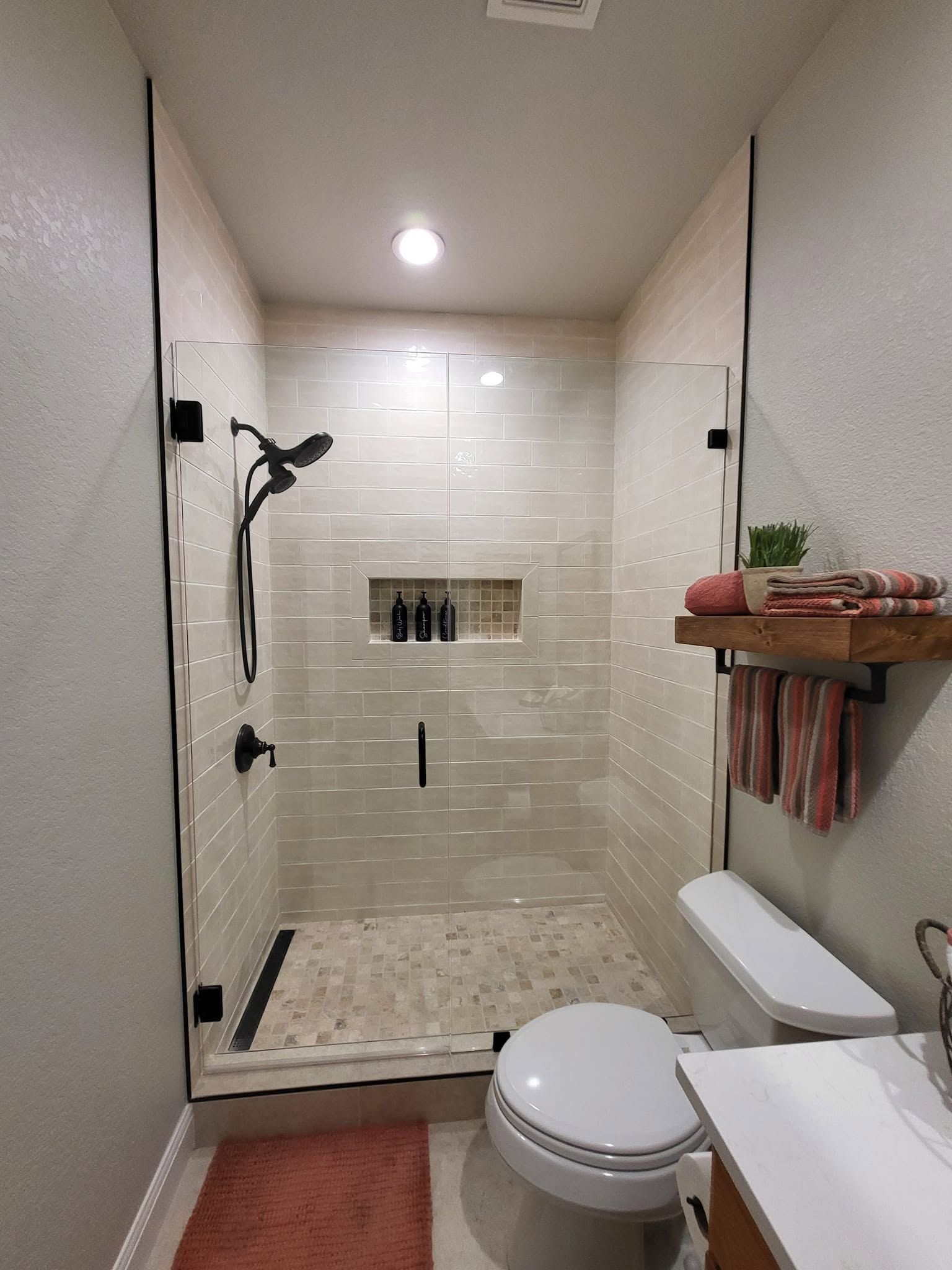 Compact modern bathroom with walk-in shower, white tile walls, and toilet in foreground