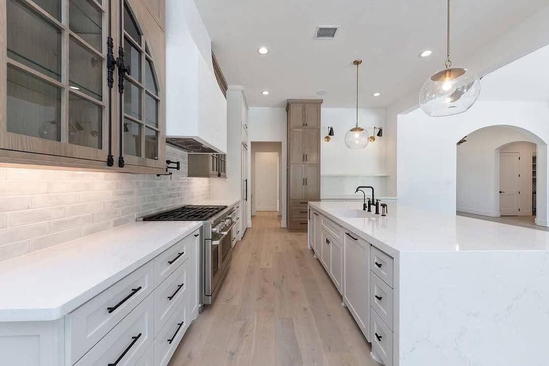 Bright modern white kitchen with light wood floors, island, pendant lights, and gray cabinets