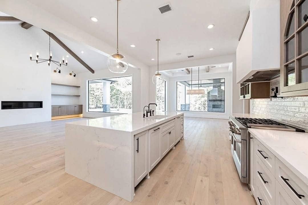 Bright modern kitchen with white island, light wood floors, and large windows