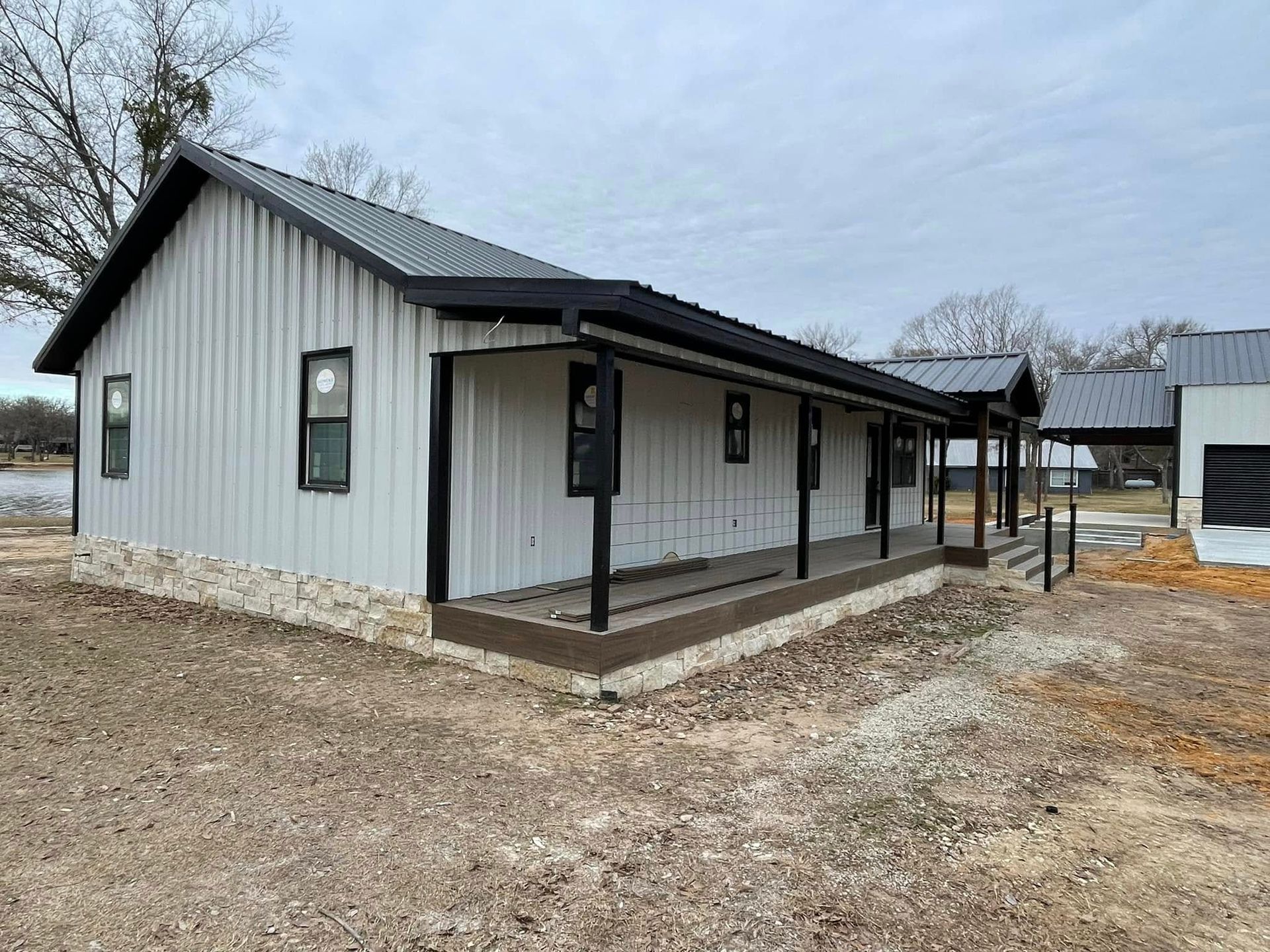 Single-story gray metal building with covered porch on a muddy lot under an overcast sky