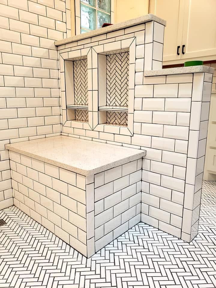White tiled kitchen with a built-in bench, herringbone floor, and two small windowed cabinets