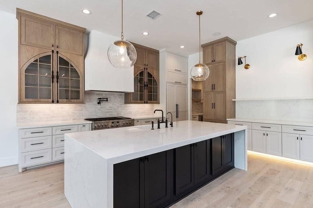 Modern kitchen with a large white island, black base cabinets, light wood accents, and pendant lights.