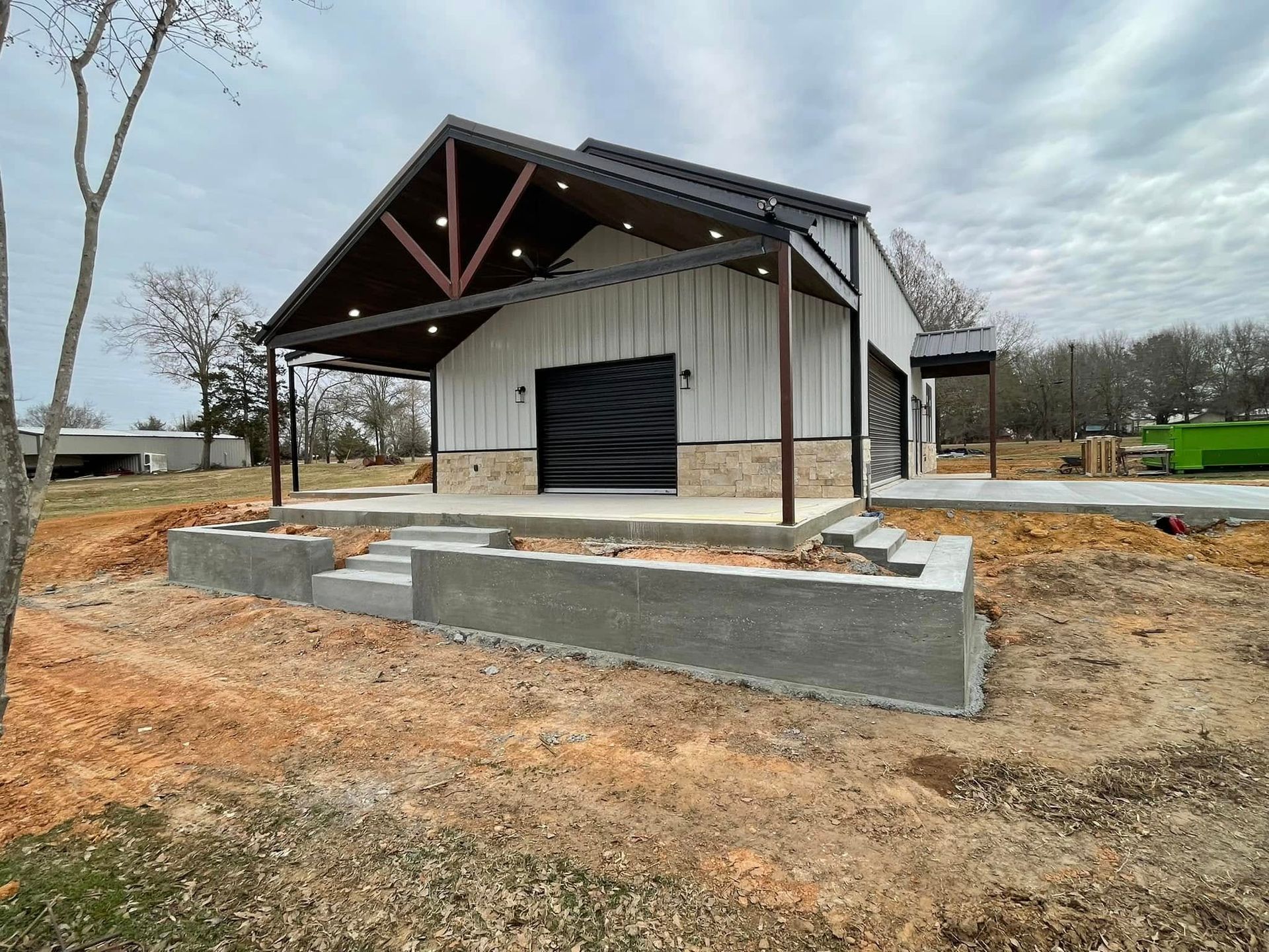 New white barn-style building with dark roof and concrete retaining wall on a dirt lot