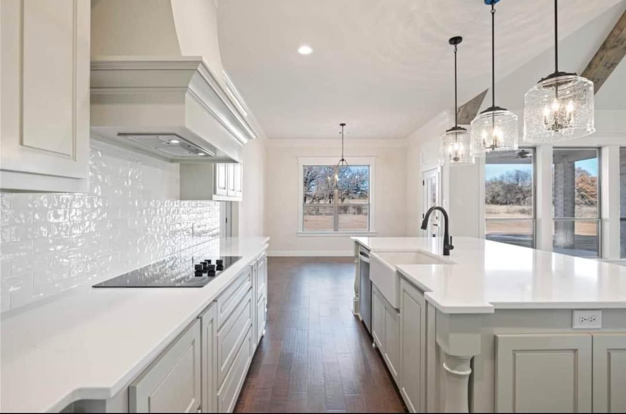 Bright modern kitchen with white cabinets, island, pendant lights, and dark wood floors