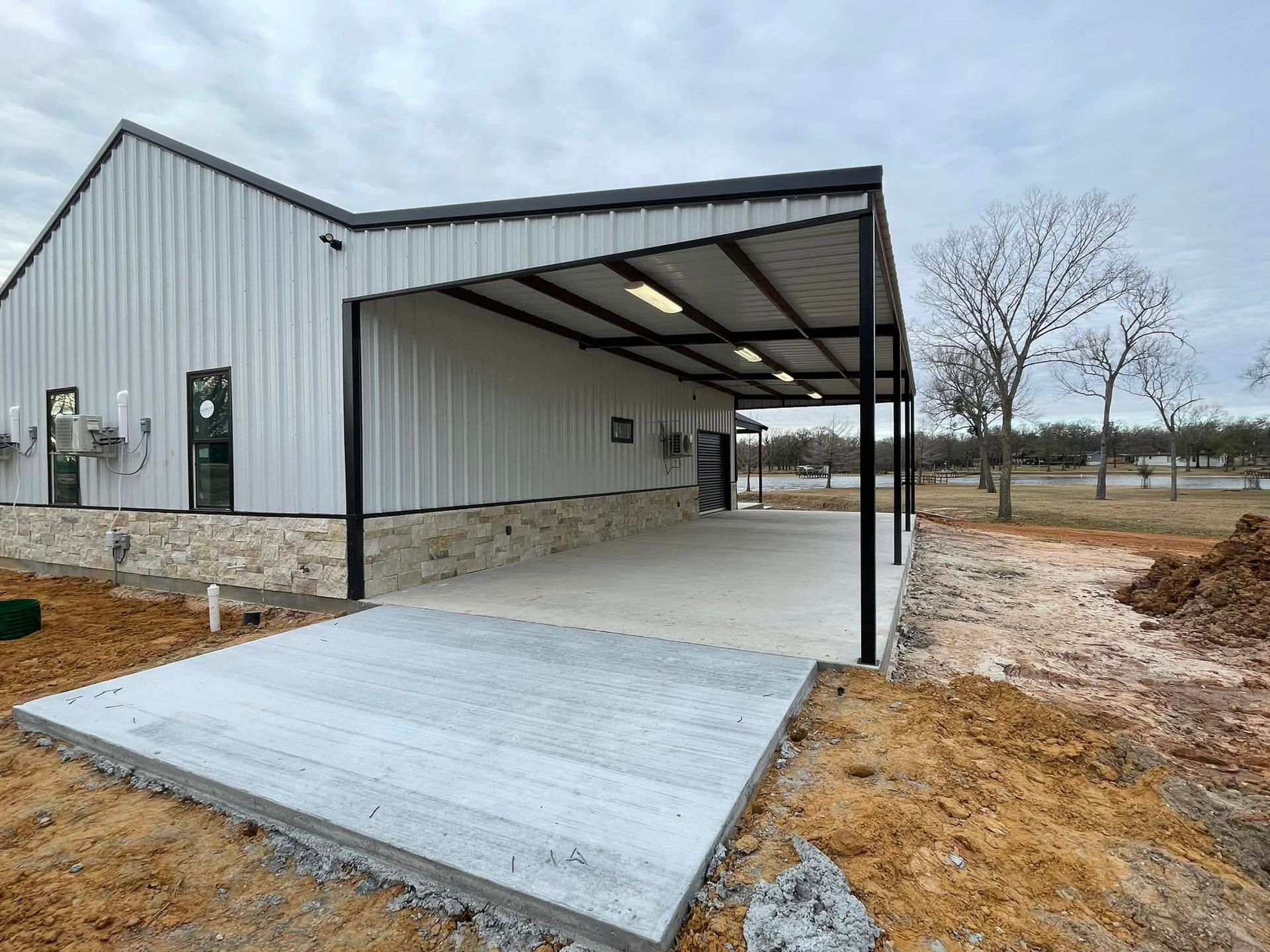 Covered concrete ramp leading to a metal-sided building under construction on a muddy lot