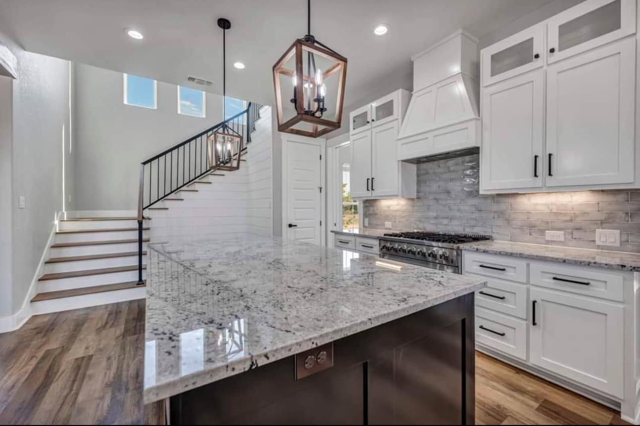 Bright modern kitchen with white cabinets, marble island, staircase, and wood floors