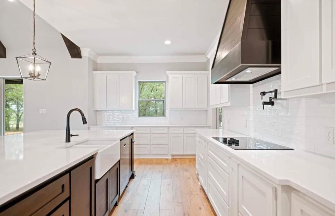 Bright modern kitchen with white cabinets, marble counters, dark island, and wood floors