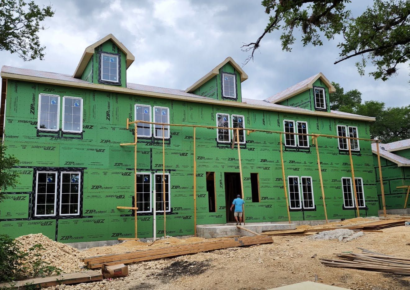 Green house under construction with workers and scaffolding under a cloudy sky