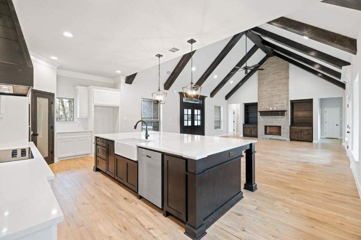 Open-concept custom kitchen and living room with vaulted ceiling, exposed black beams and large island