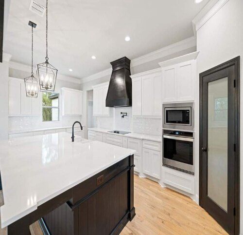 Bright modern kitchen with white cabinets, black island, stainless appliances, and hardwood floors
