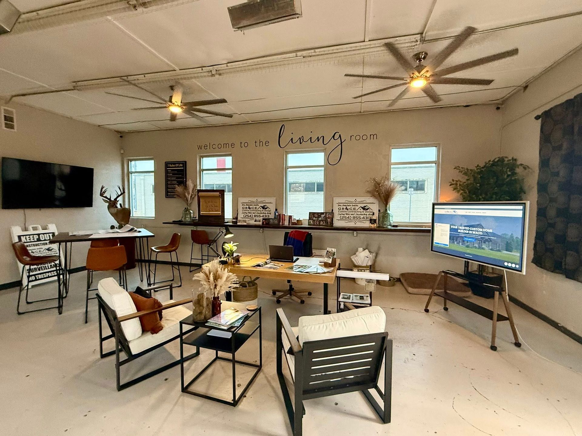 Modern home office with desks, chairs, ceiling fans, wall art, and a large TV on a stand