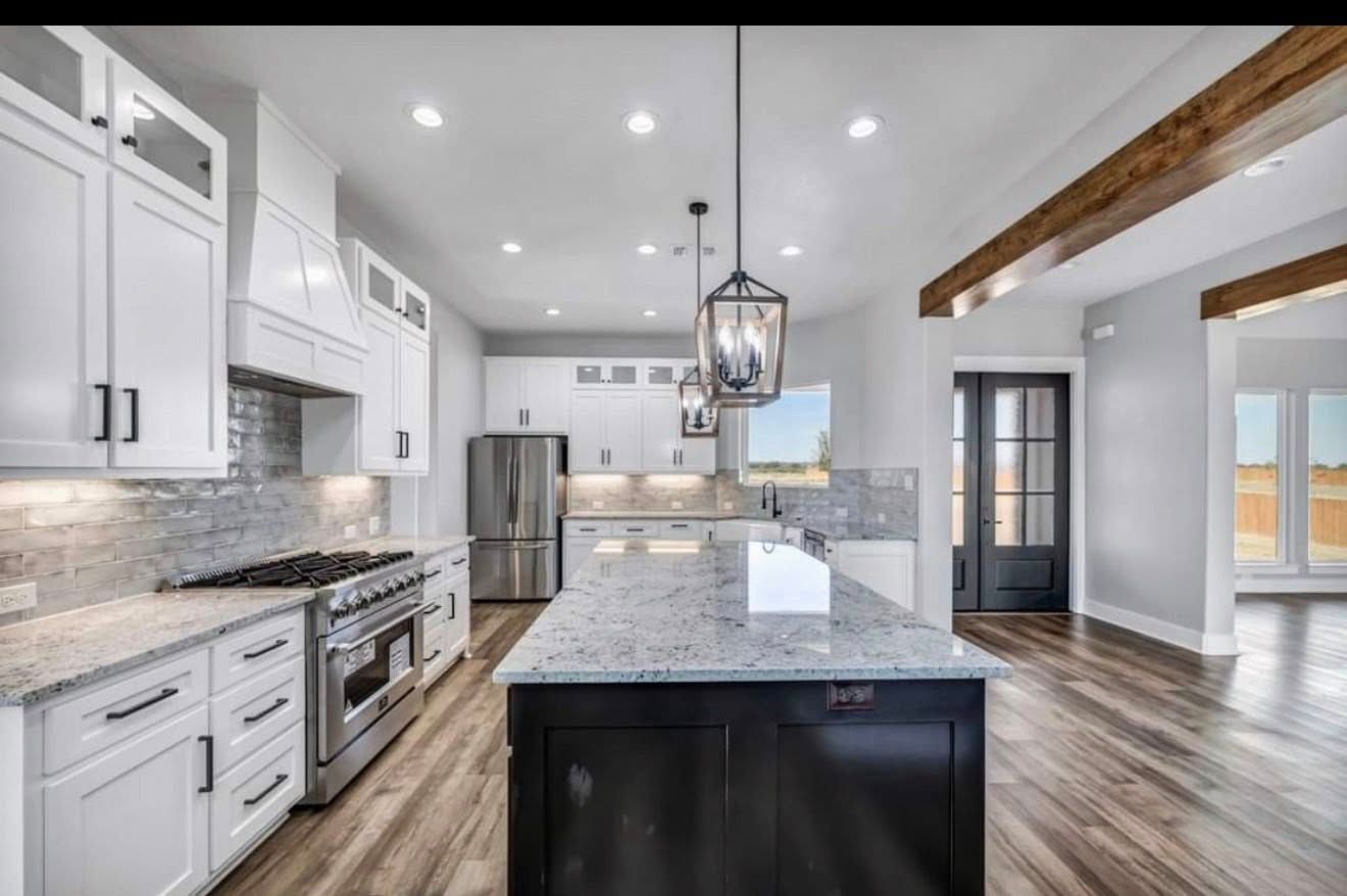 Bright modern kitchen with white cabinets, marble island, stainless steel appliances, and wood floors