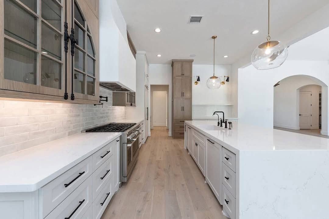 Bright modern kitchen with white cabinets, light wood floors, marble island, and pendant lights