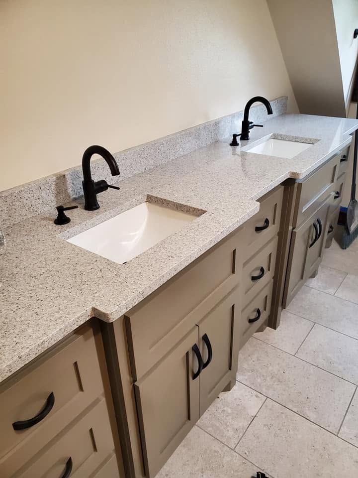 Double-sink bathroom vanity with beige cabinets, black faucets, and light speckled countertops