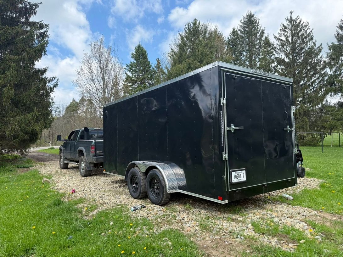 Black enclosed trailer hitched to a dark pickup truck on a gravel drive beside green grass and trees. | 814 Truck & Equipment Services LLC